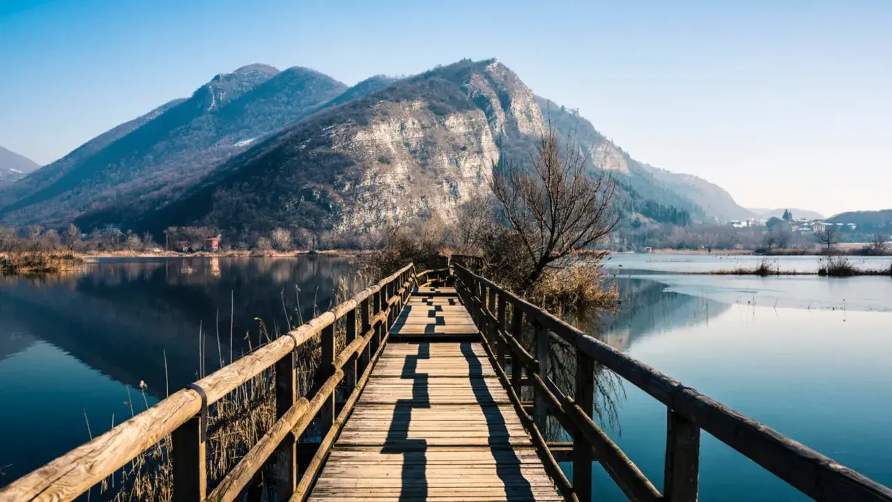 Passerella in legno su lago calmo, montagne sullo sfondo. Un luogo incantevole per scoprire cosa vedere in Franciacorta.