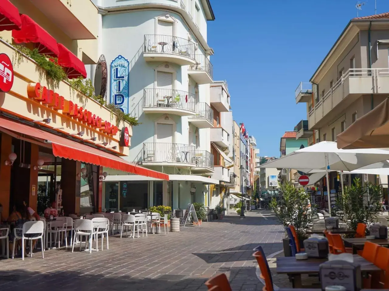 Passeggiata serale a Gabicce Mare: tavolini all'aperto di un caffè, hotel Lido e negozi colorati.