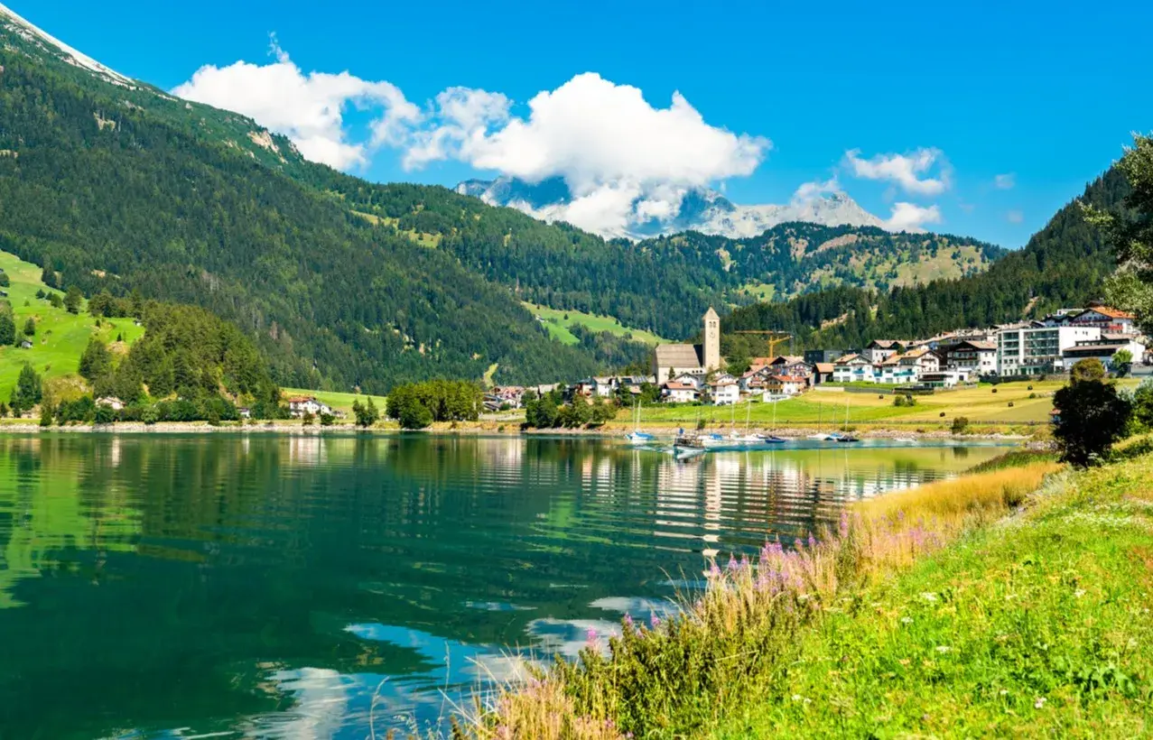 Incantevole lago alpino con barche a vela, circondato da verdi montagne e pittoreschi borghi Trentino Alto Adige.