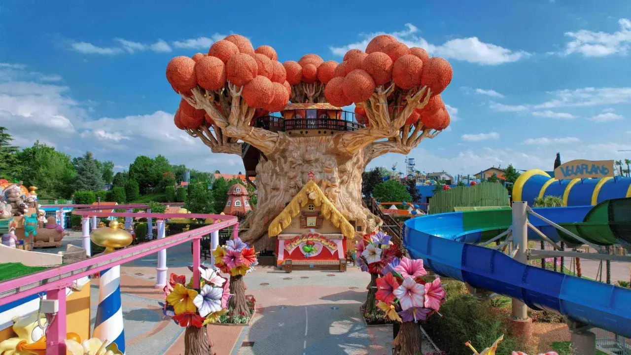 Un magico parco divertimenti in Italia con un albero gigante, scivoli acquatici e giostre colorate.