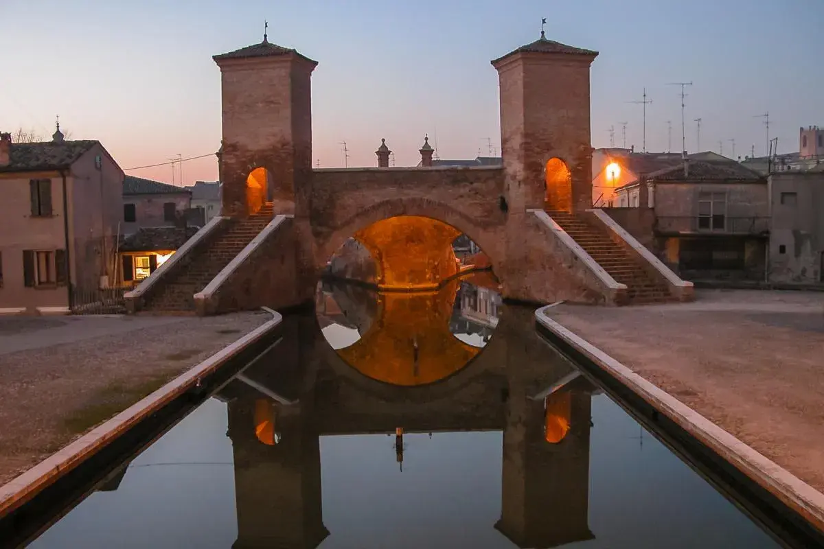 Ponte di barche a Comacchio, uno dei borghi medievali vicino a Ferrara, con le sue torri illuminate e il riflesso sull'acqua.