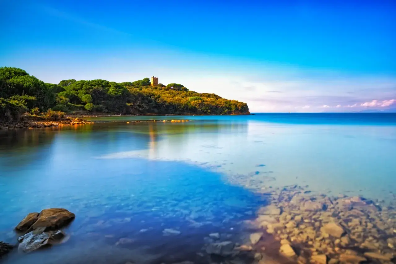 Torre medievale su una collina verdeggiante che si affaccia su acque cristalline, una delle punta ala spiagge più belle.