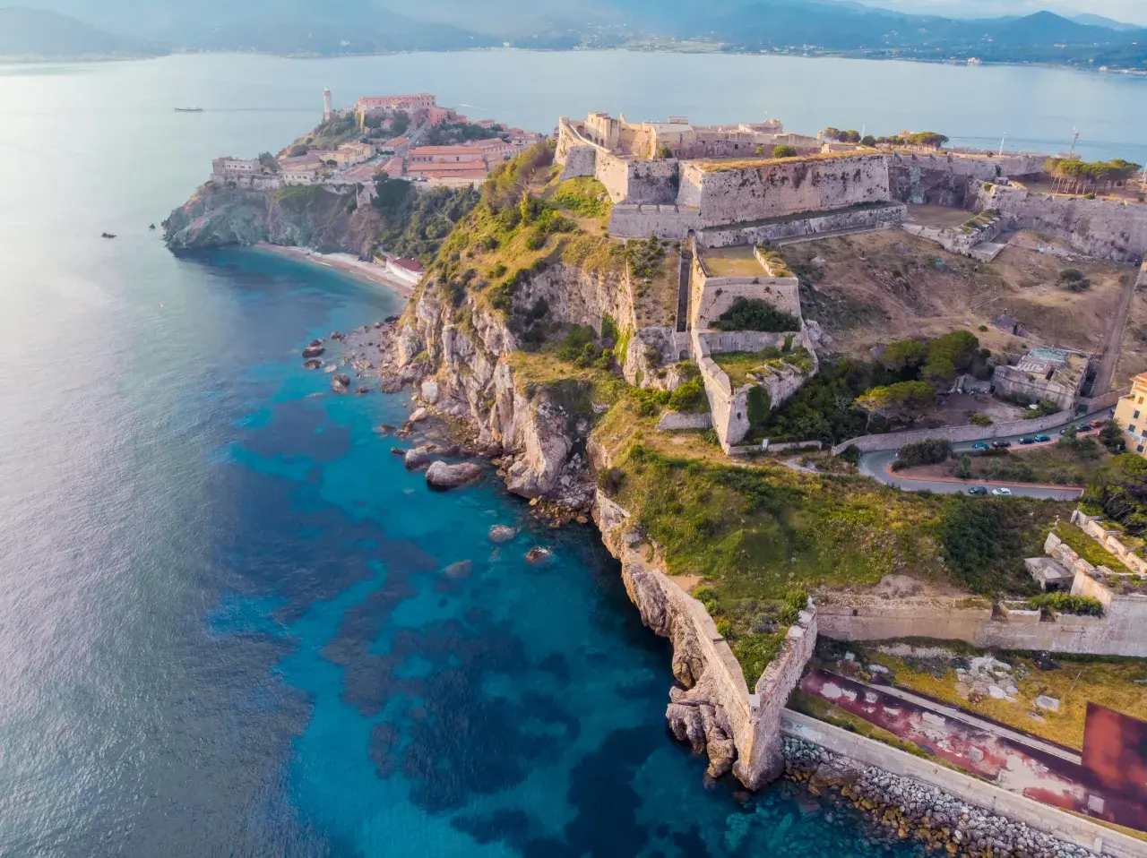 Fortificazioni storiche su una costa rocciosa con mare blu intenso. Un'idea per cosa visitare in Toscana in 2 giorni, tra storia e natura.