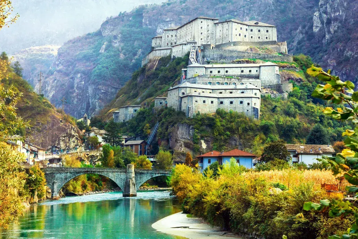 Fortezza imponente su un colle, con un fiume turchese e un ponte ad arco. Un paesaggio da fiaba tra Piemonte e Valle d'Aosta.