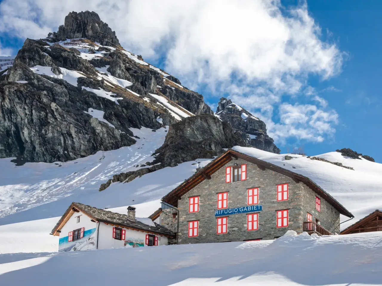 Rifugio Gabiet, uno dei rifugi valle d'Aosta facili, immerso nella neve con montagne imponenti sullo sfondo.