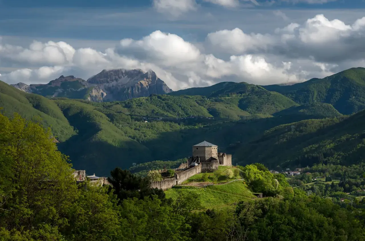 Roccia fortificata nella Garfagnana, dove si trova un castello medievale su una collina verdeggiante, con montagne sullo sfondo.