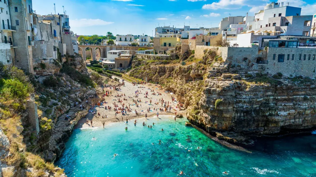 Una baia con spiaggia affollata e case bianche a picco sul mare turchese, una delle splendide spiagge vicino Bari.