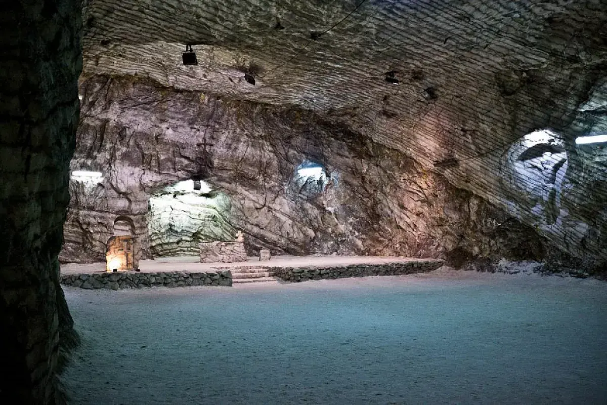 Interno della cattedrale di sale di Realmonte, con pareti rocciose stratificate e un altare illuminato.