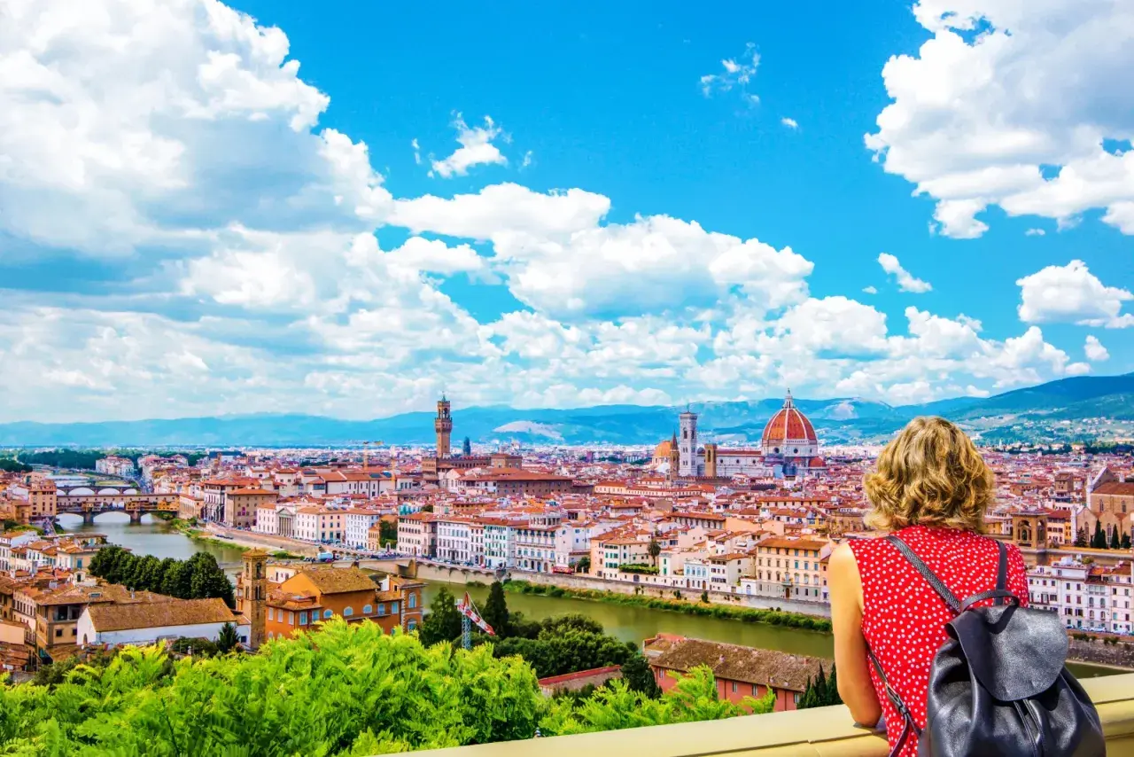 Una donna ammira il panorama di Firenze, la capitale della Toscana, con il Duomo e il Ponte Vecchio sotto un cielo azzurro e nuvoloso.