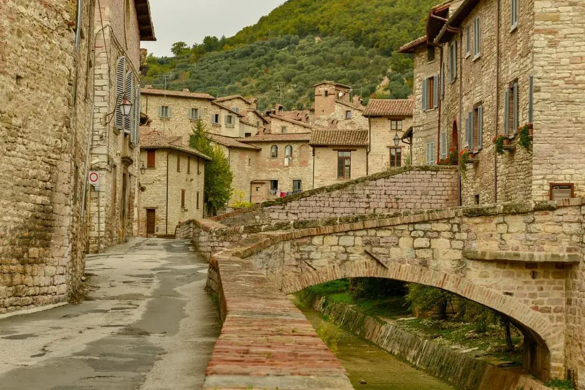 Antica via acciottolata con un ponte in pietra su un ruscello, circondata da case in pietra. Un'immagine perfetta dei borghi da visitare in Umbria.