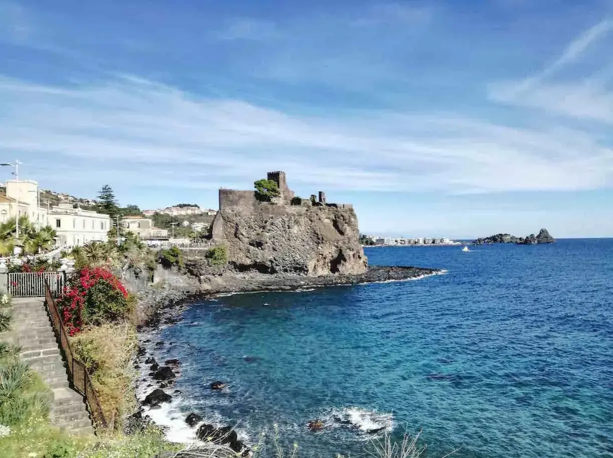 Castello normanno su scogliera lavica, un gioiello tra le cose da vedere a Catania e dintorni. Mare azzurro e case bianche.