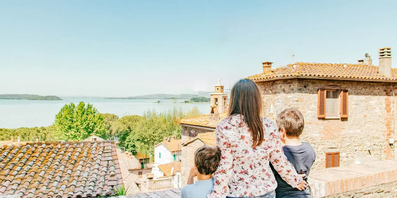 Una madre e due bambini ammirano un lago e un borgo italiano, scoprendo luoghi magici per bambini in Italia.