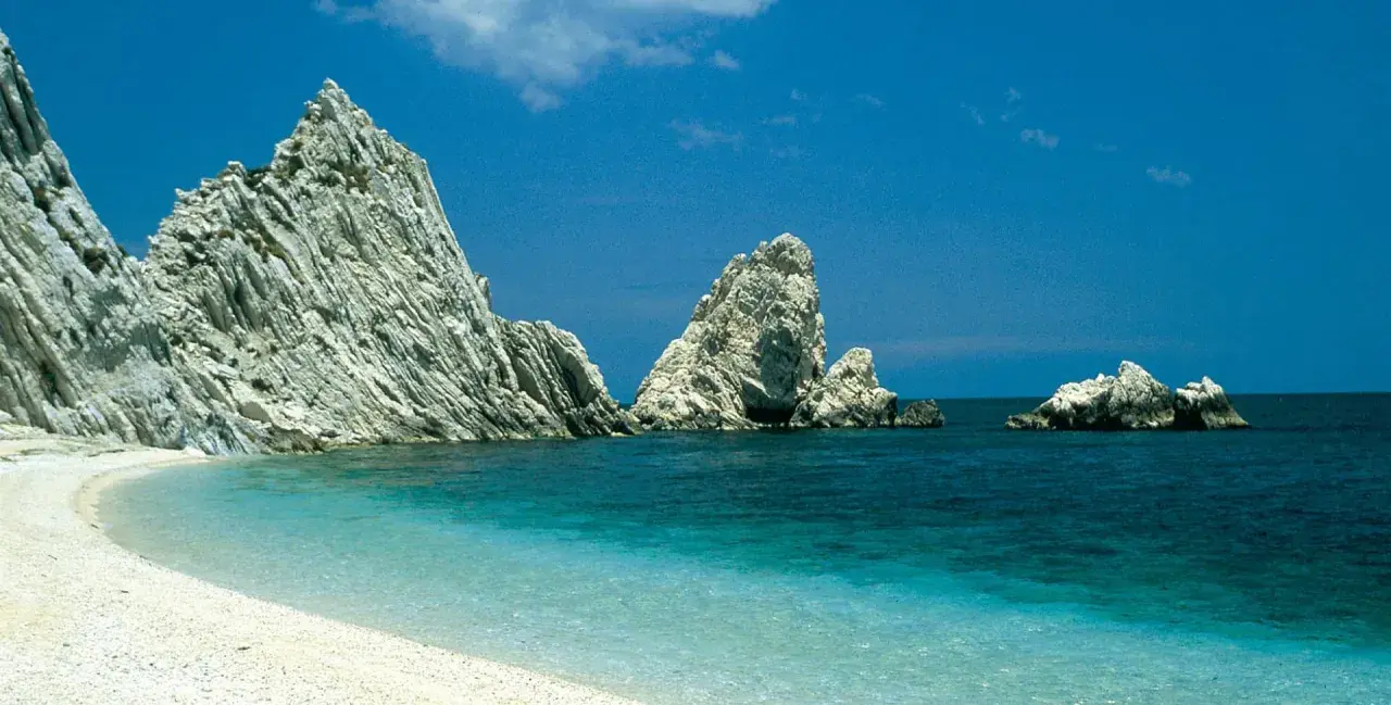 Spiaggia bianca e mare cristallino, rocce imponenti emergono dall'acqua turchese. Un angolo di paradiso nelle Marche, mare bello da cartolina.