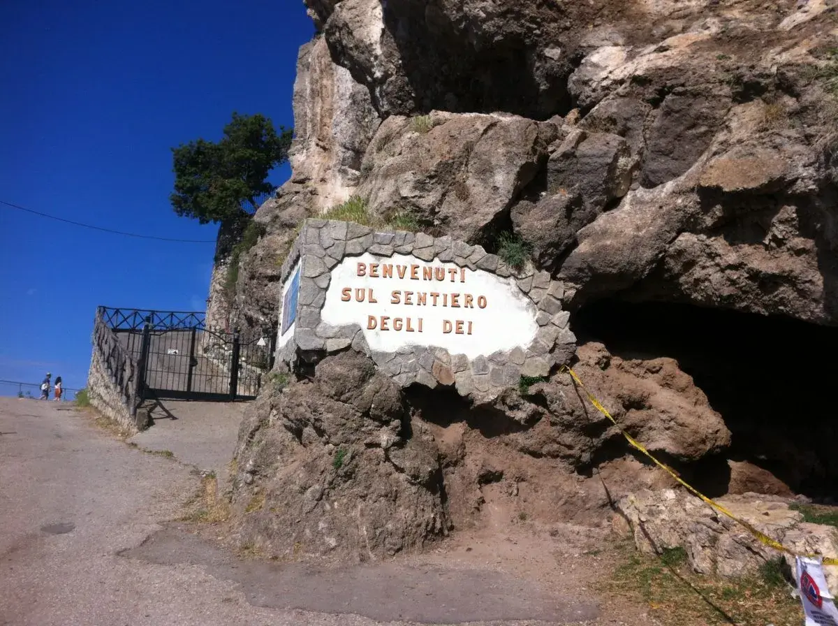 Benvenuti sul Sentiero degli Dei, un'iconica insegna incastonata nella roccia, con un cancello e un sentiero che invitano all'avventura.