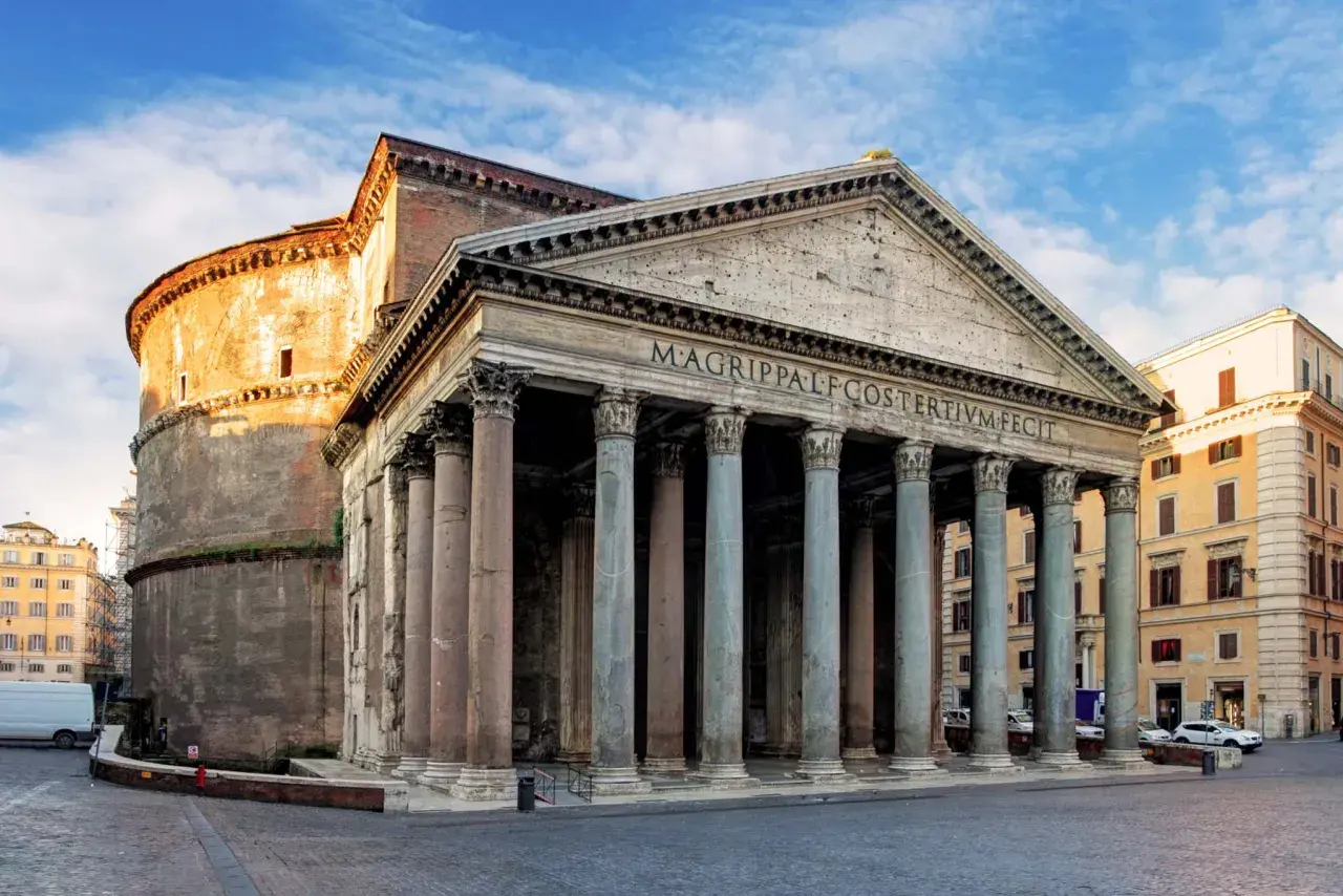 Il Pantheon, una delle chiese particolari di Roma, con il suo portico colonnato e la cupola imponente, si staglia sotto un cielo azzurro.