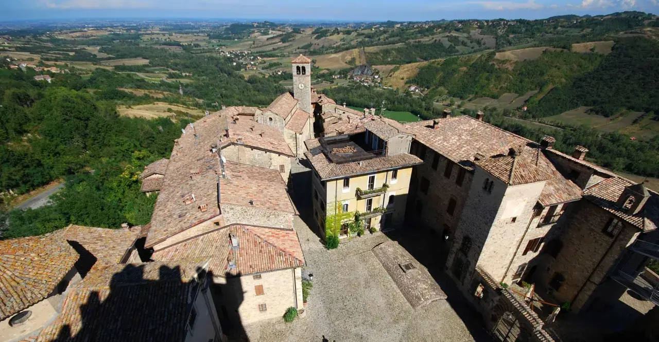 Vista aerea del borgo di Vigoleno, con tetti in cotto e un campanile che domina il paesaggio collinare.