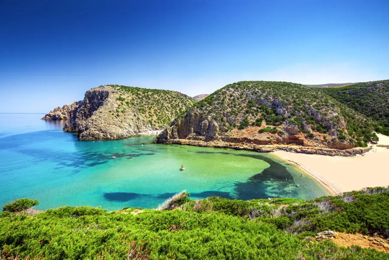 Spiagge della Sardegna: caletta con acque cristalline, sabbia dorata e macchia mediterranea. Un angolo di paradiso che risponde alla domanda: quali sono le spiagge più belle della Sardegna?
