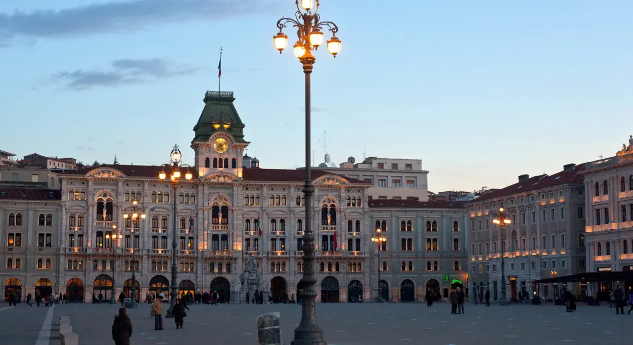 Piazza Unità d'Italia a Trieste, con i suoi palazzi illuminati e un cielo crepuscolare.