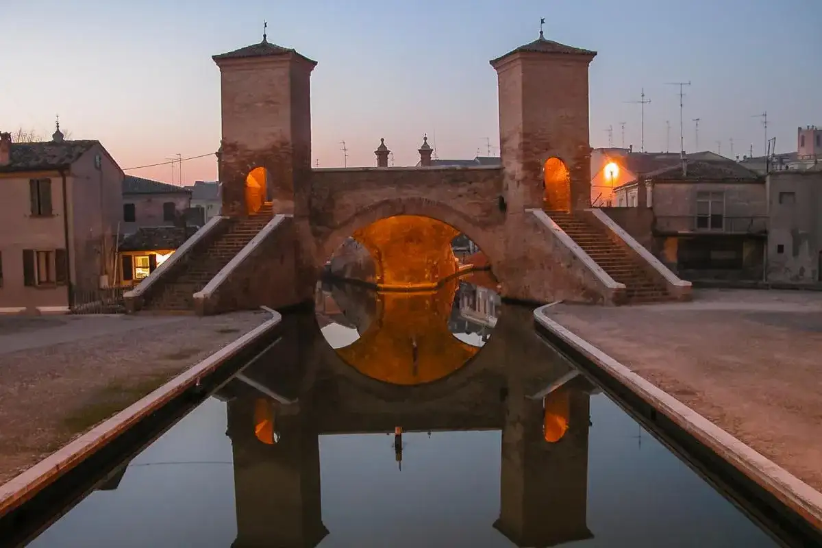 Ponte di barche a Comacchio, uno dei borghi medievali vicino a Ferrara, con le sue torri illuminate e il riflesso sull'acqua.