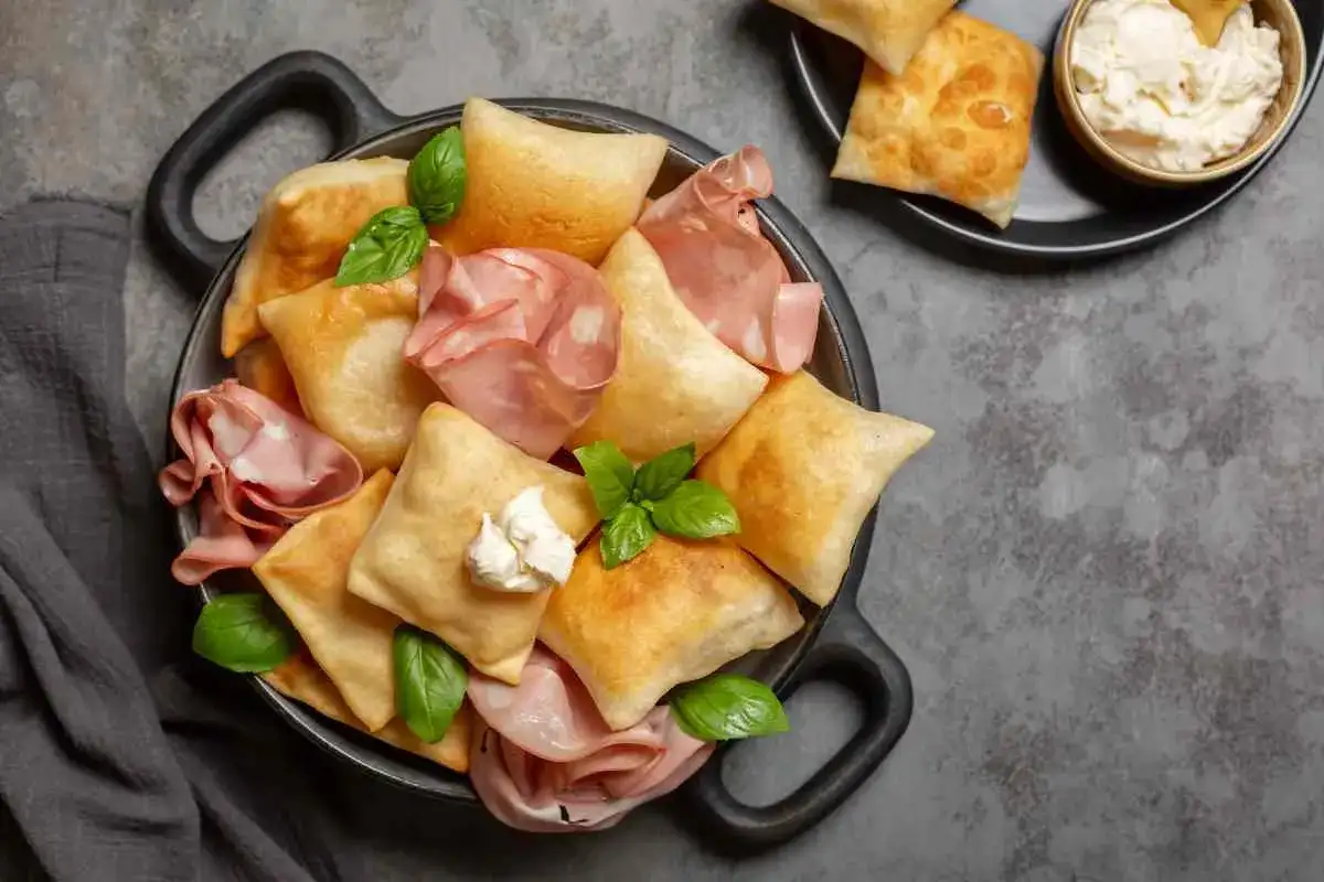 Fritti e ripieni, ecco cosa mangiare a Parma: gnocco fritto con salumi e formaggio cremoso, un'esplosione di gusto.