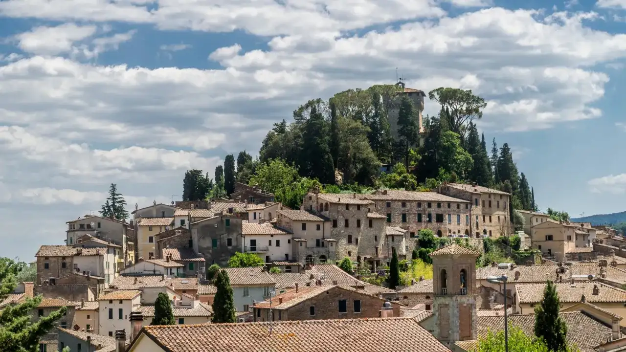 Panoramica di Cetona, un borgo toscano arroccato su una collina, con case in pietra e tetti in cotto sotto un cielo nuvoloso.