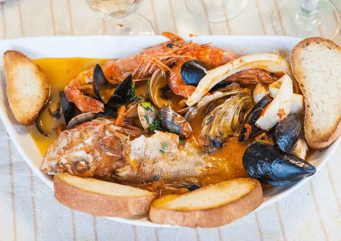 Un ricco piatto di pesce misto, con crostacei, molluschi e pesce intero, servito con pane tostato. Perfetto per scoprire cosa mangiare a Ravenna.
