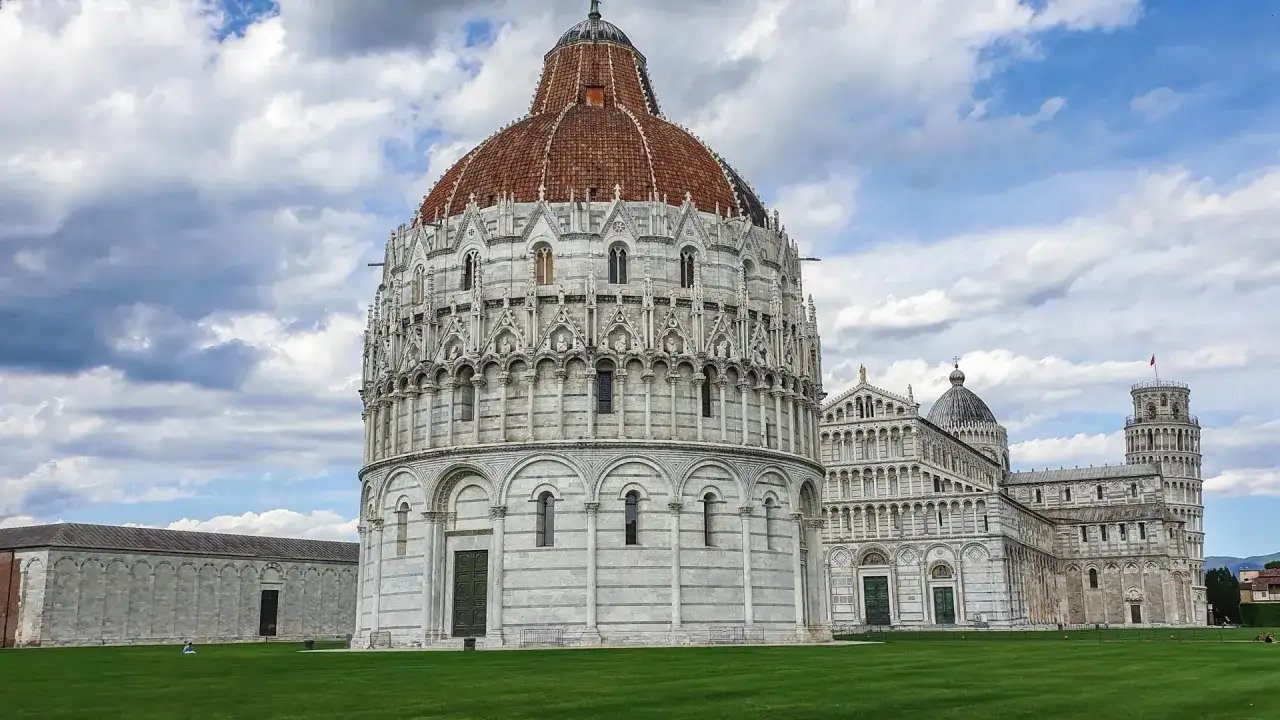 Il Battistero e la Torre Pendente nel centro di Pisa, sotto un cielo nuvoloso.