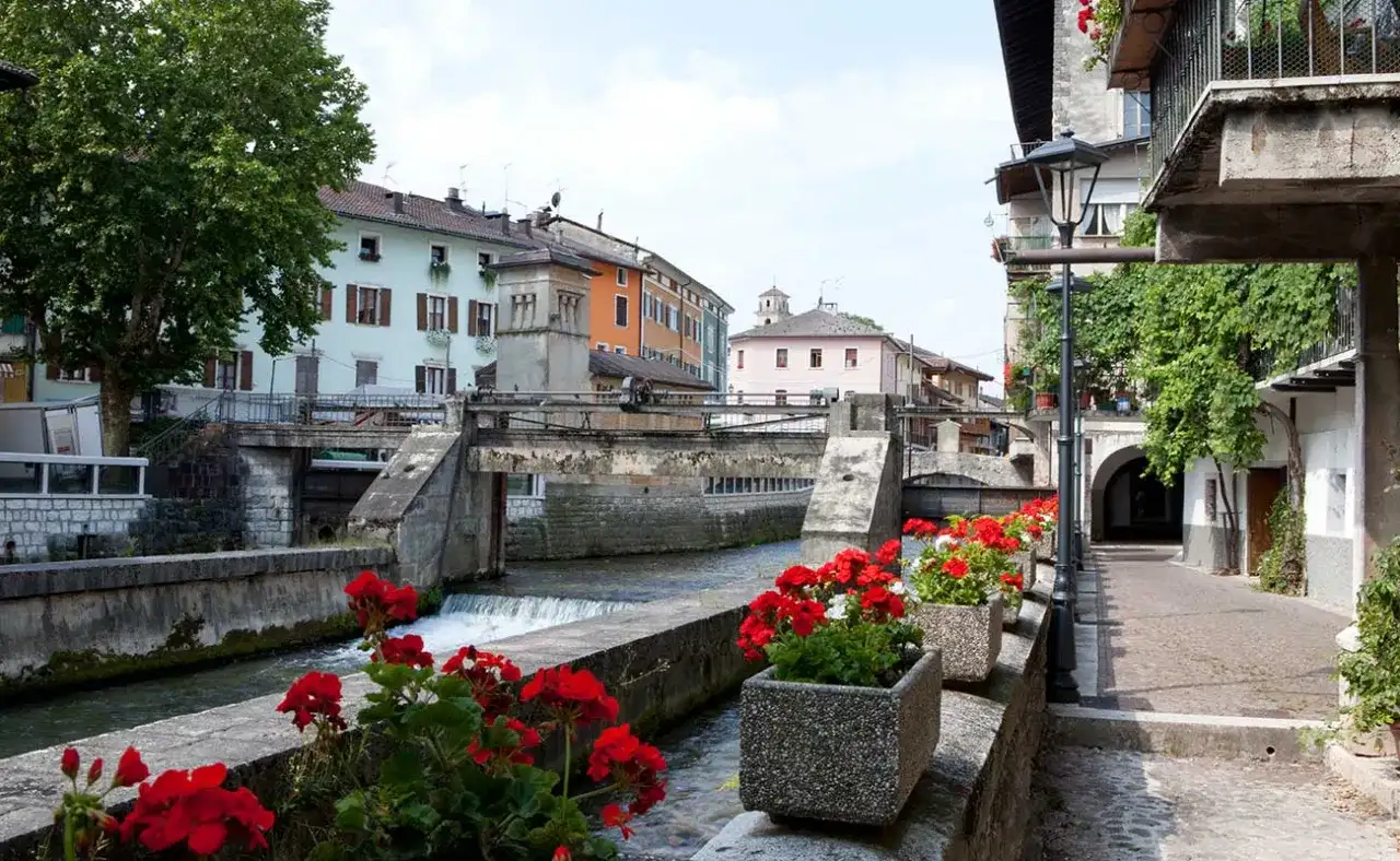 Un pittoresco canale attraversa il borgo Val Sugana, fiancheggiato da case colorate e gerani rossi in fiore.