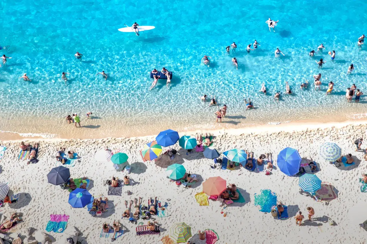 Vacanze estive sulle spiagge di sabbia con fondale basso in Calabria. Gente che si rilassa al sole e nuota nell'acqua cristallina.