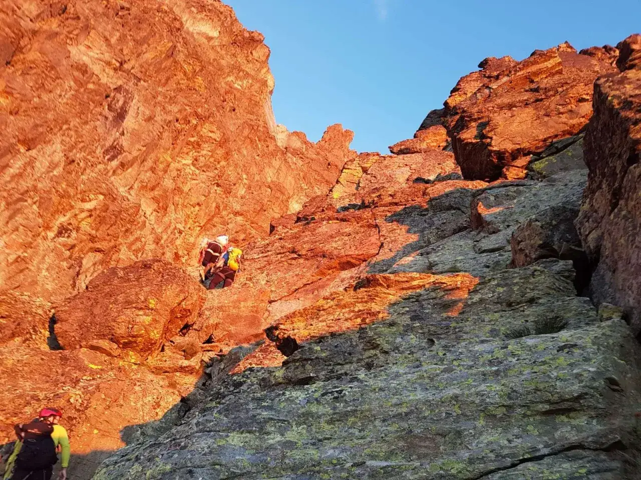 Alpinisti scalano roccia infuocata dal sole al tramonto, lungo la via normale del Monviso.