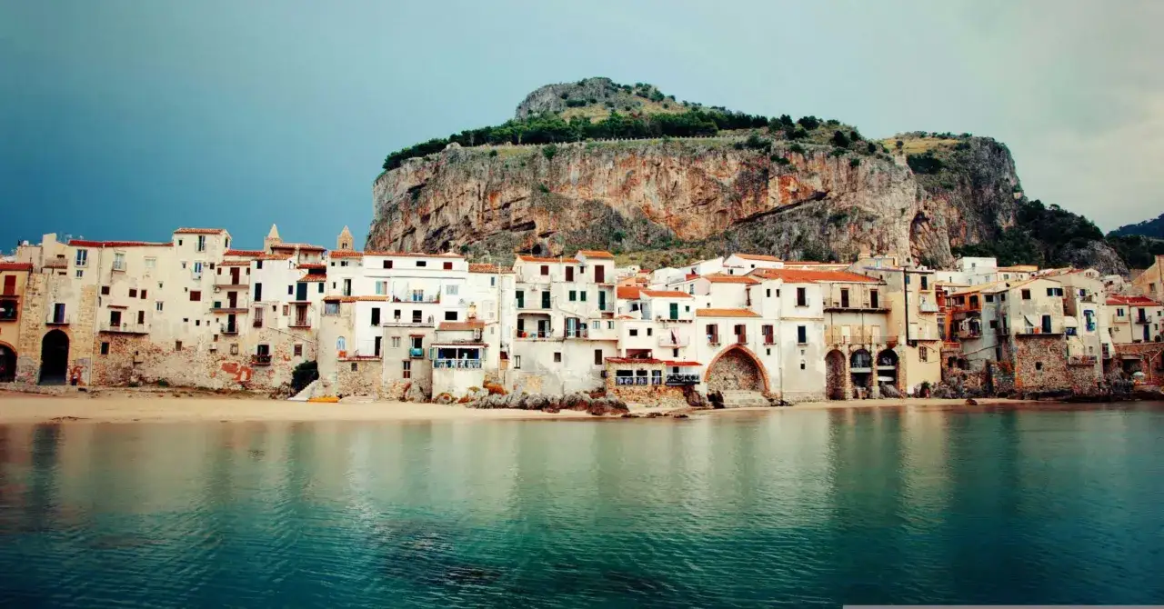 Un incantevole borgo da visitare in Sicilia, con case bianche a picco sul mare e una rocca imponente sullo sfondo.