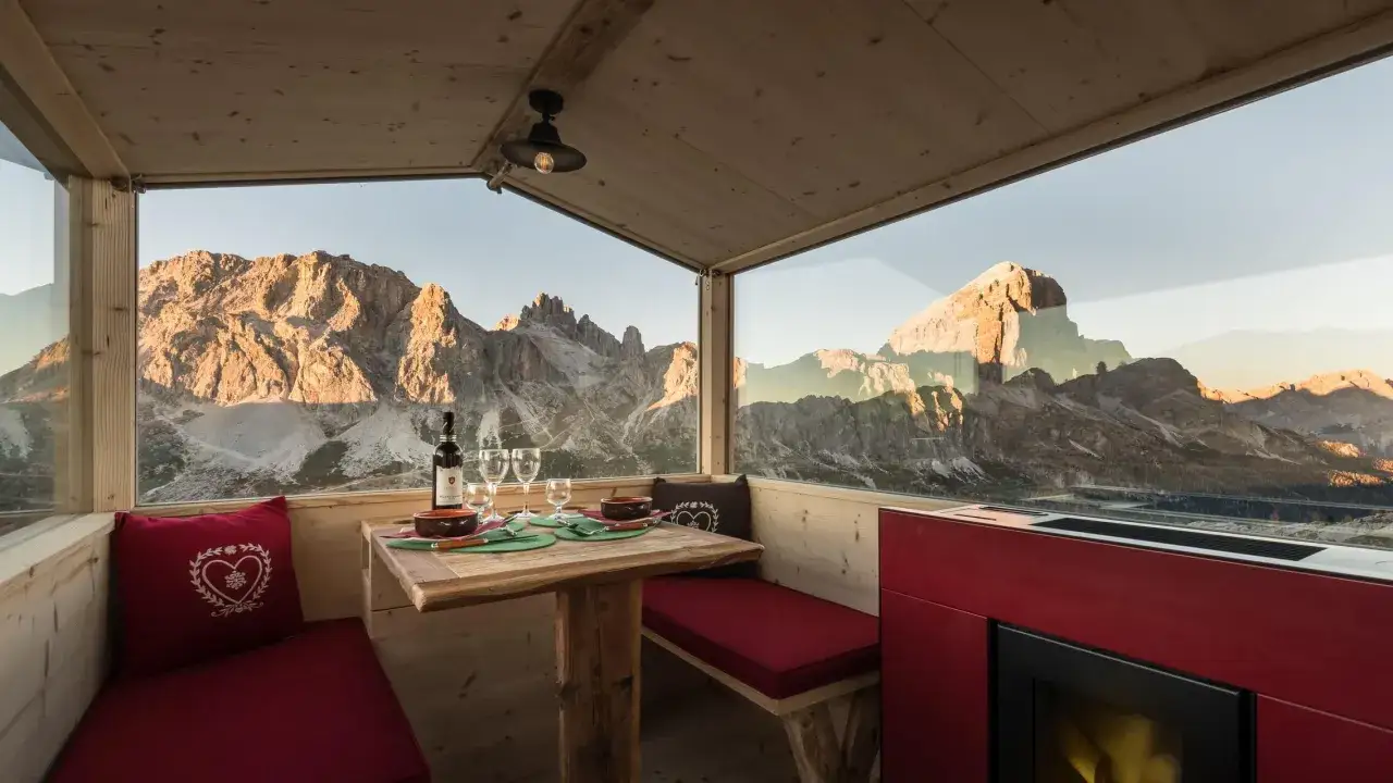 Un tavolo apparecchiato con vino e bicchieri, pronto per una cena romantica in uno dei rifugi di montagna più suggestivi, con vista mozzafiato sulle vette al tramonto.