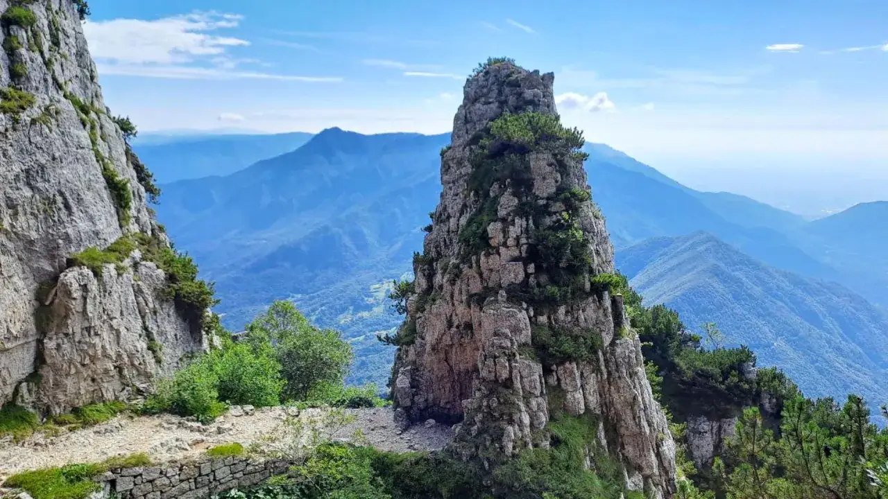 Sentiero roccioso tra montagne verdi, ideale per passeggiate in Veneto. Un picco imponente domina il paesaggio.