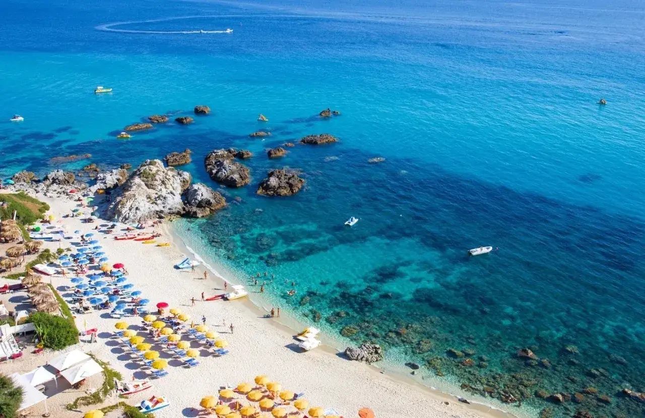 Spiagge di sabbia con fondale basso in Calabria, bagnate da un mare cristallino. Ombrelloni colorati e gente che si gode il sole.