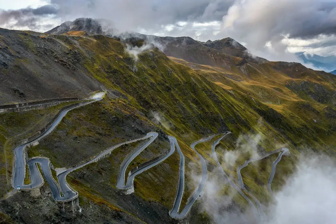 Serpentine strade di montagna, un elenco di passi alpini italiani che si snodano tra nuvole e pendii verdi.