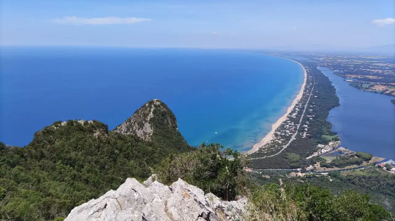 Vista mozzafiato dal promontorio del Circeo: mare azzurro, spiaggia dorata e un lago serpeggiante tra la vegetazione.