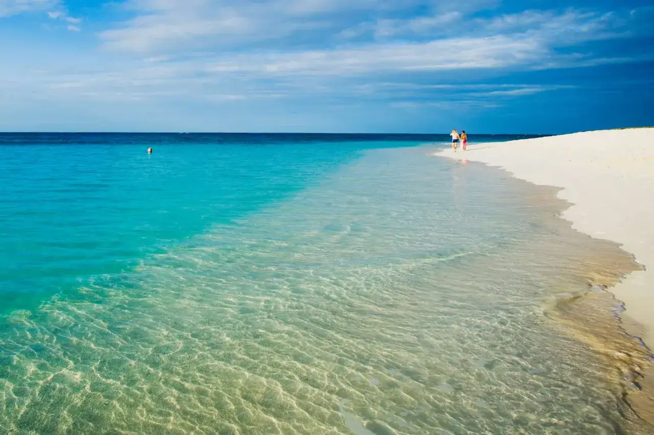 Coppia passeggia su una spiaggia bianca, bagnata da un mare cristallino che sembra il mare più bello del mondo.