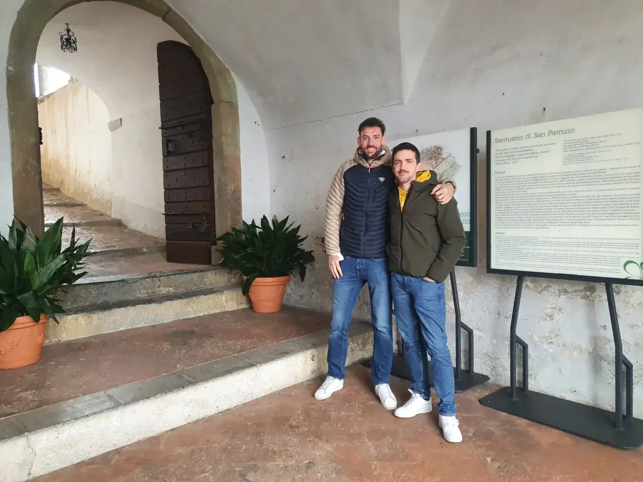 Due amici visitano il Santuario di San Patrizio, un luogo storico con un'antica porta e pannelli informativi.