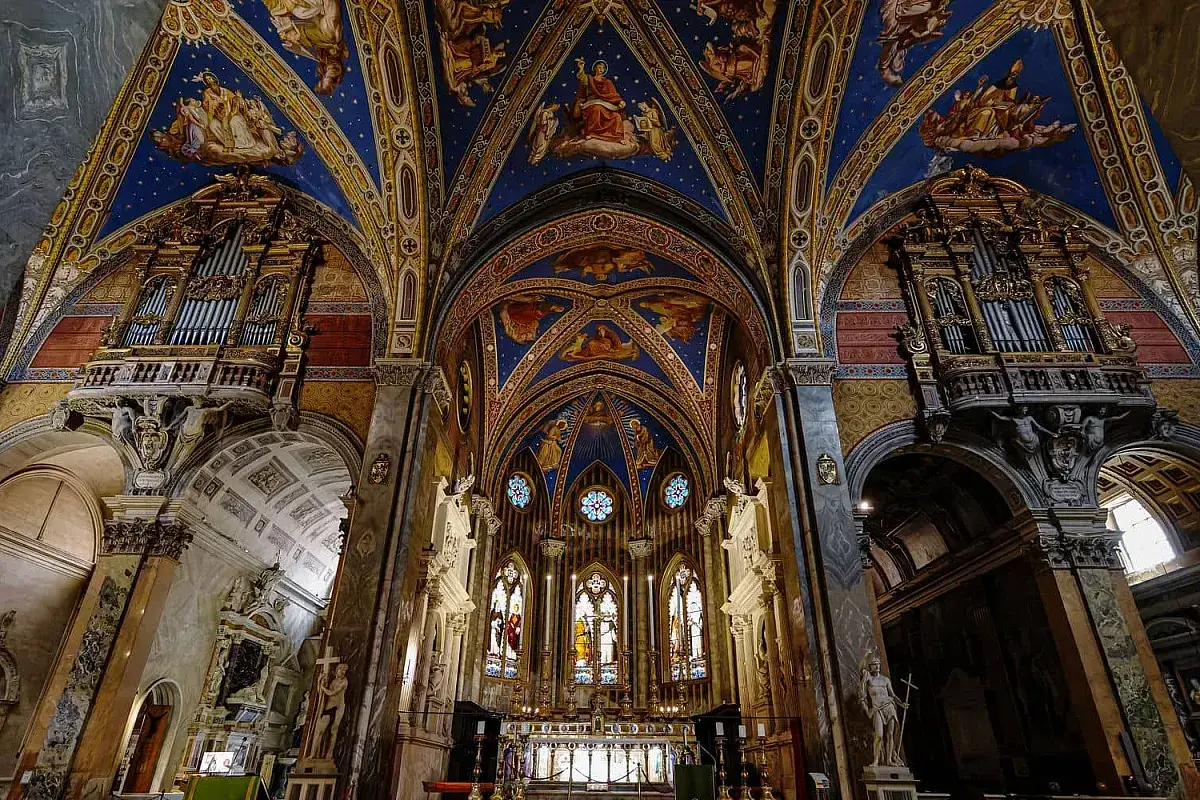 Interno di chiese particolari a Roma: volte affrescate con angeli, organi dorati e vetrate colorate creano un'atmosfera celestiale.