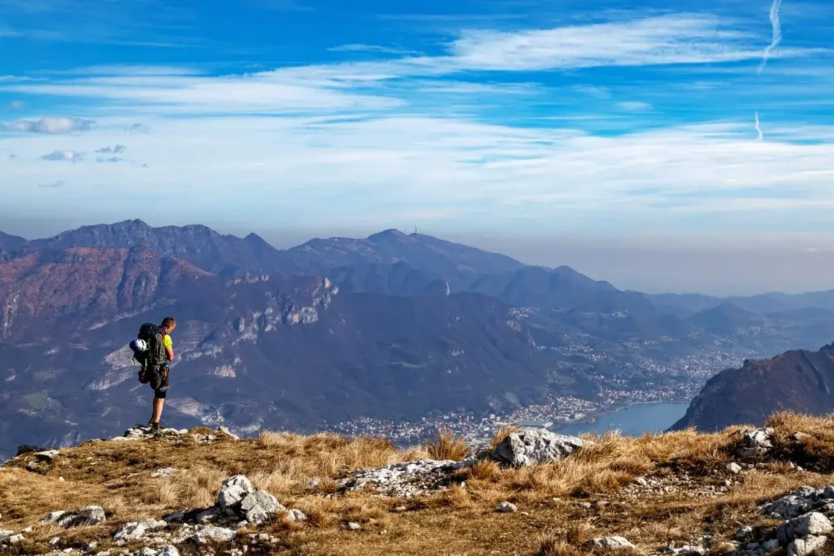 Escursionista con zaino ammira il panorama montano, un luogo ideale per passeggiate in montagna vicino a Milano.