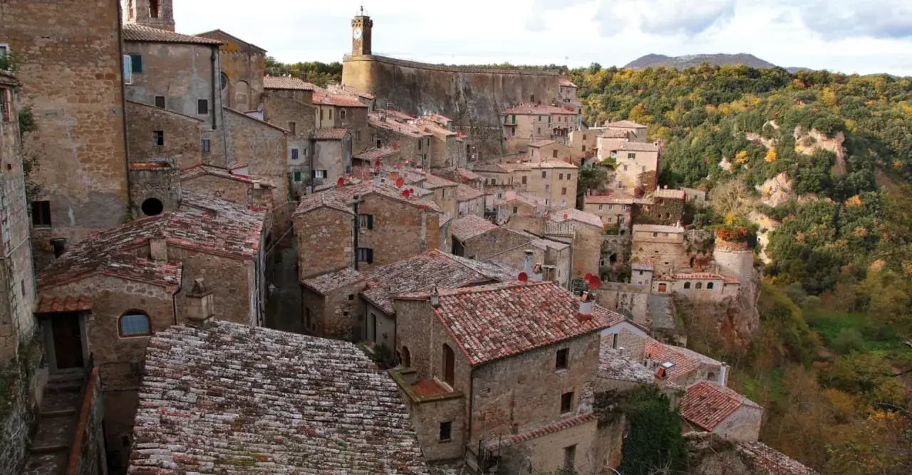 Sorano, un borgo medievale arroccato su una rupe tufacea, con case in pietra e tetti rossi che si fondono con il paesaggio collinare.