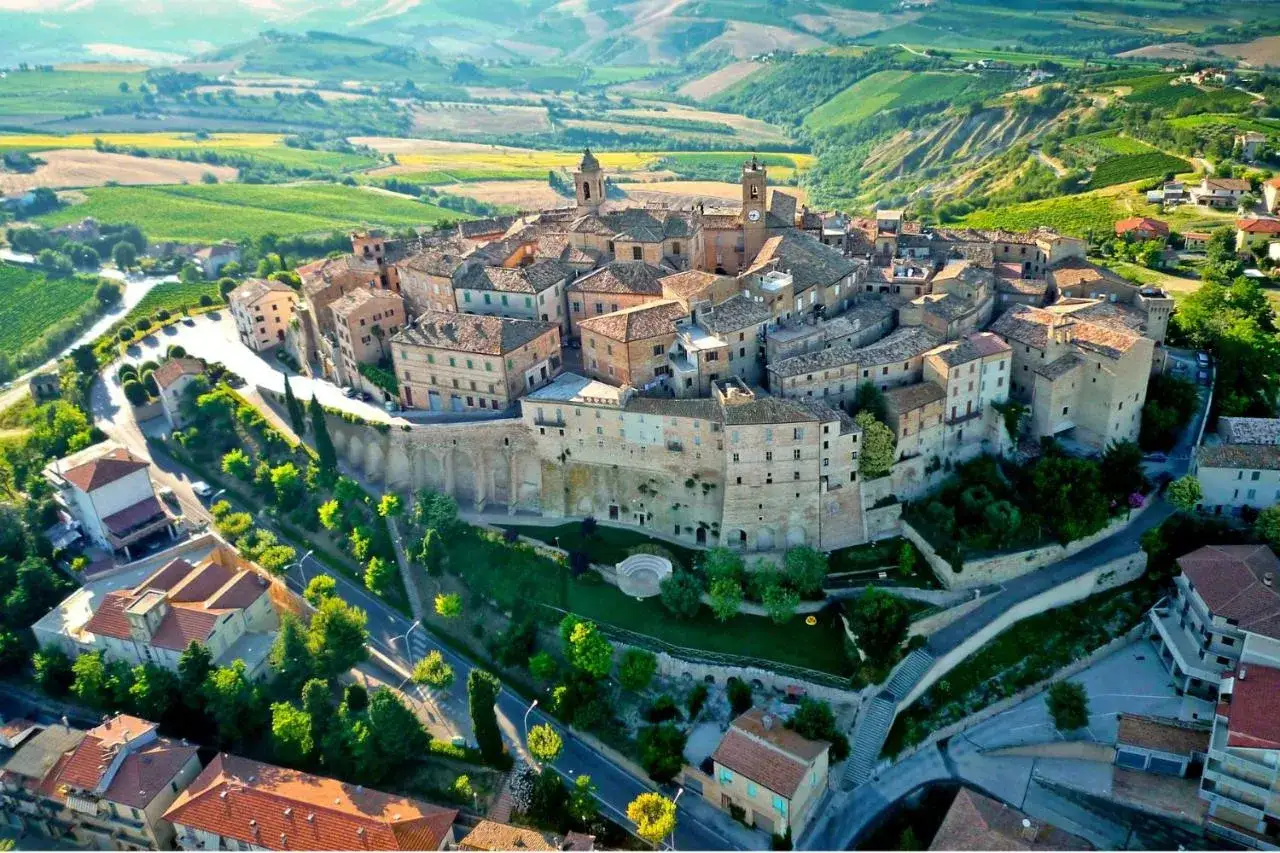 Un borgo medievale arroccato su una collina, tra colline verdi e campi coltivati. Un gioiello tra i borghi da visitare vicino Ascoli Piceno.
