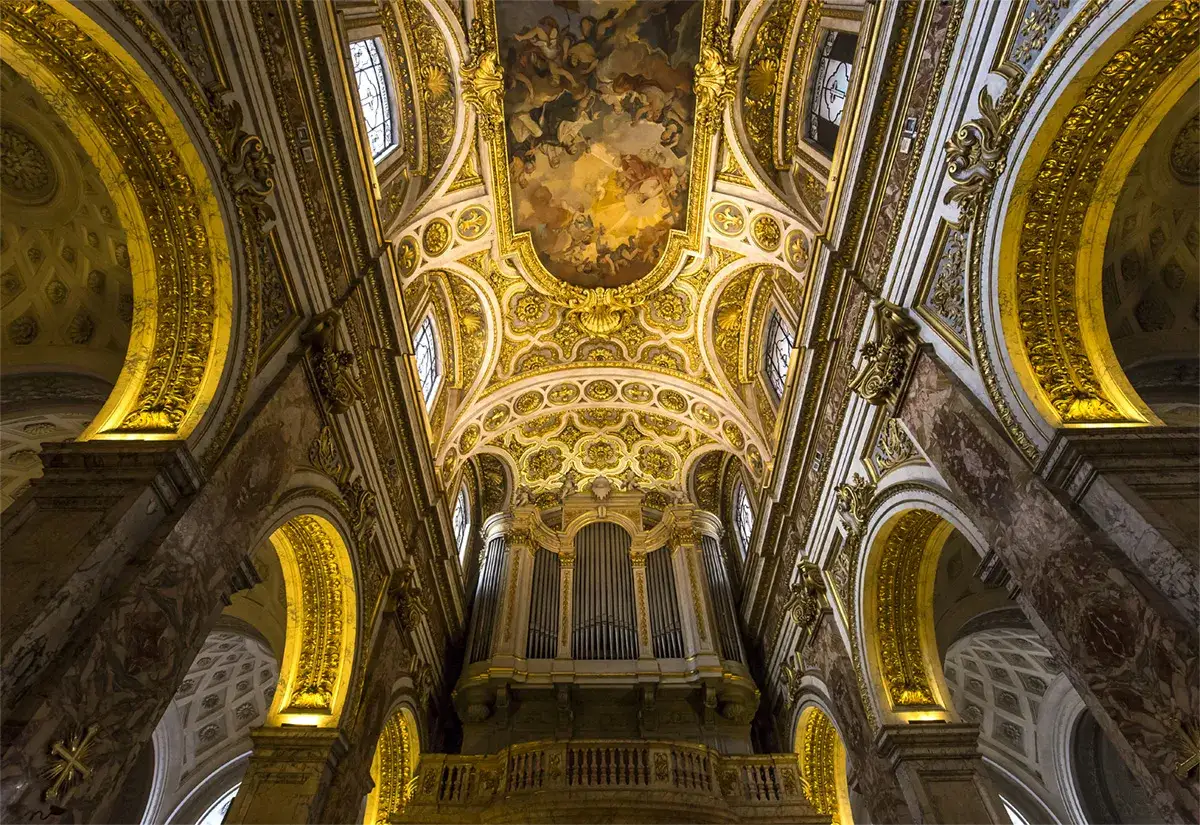 Interni sfarzosi di una chiesa a Roma, con soffitto affrescato, organo imponente e decorazioni dorate. Un esempio delle magnifiche chiese da vedere a Roma.