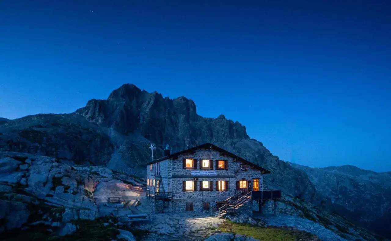Rifugio Tita Secchi, uno dei rifugi Val Camonica facili, illuminato al crepuscolo con montagne maestose sullo sfondo.