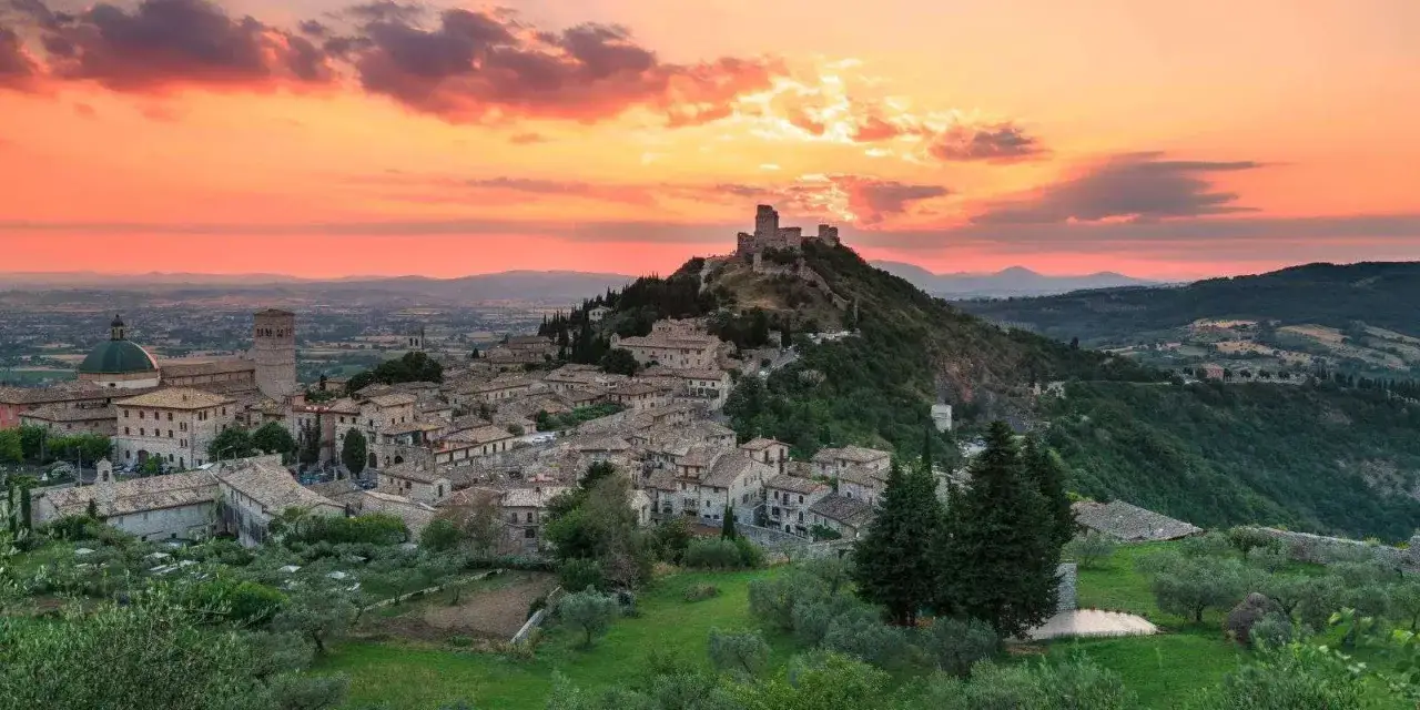 Assisi, uno dei borghi da visitare in Umbria, si staglia al tramonto con la sua Rocca Maggiore.