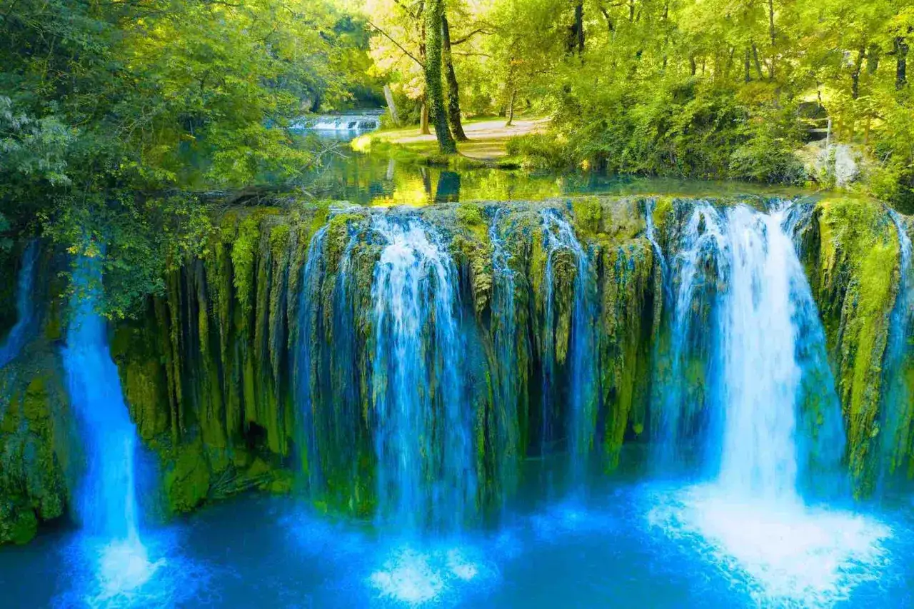 Cascata rigogliosa, un angolo di paradiso per i tuoi cammini in Toscana. L'acqua azzurra scende tra rocce verdi e alberi lussureggianti.