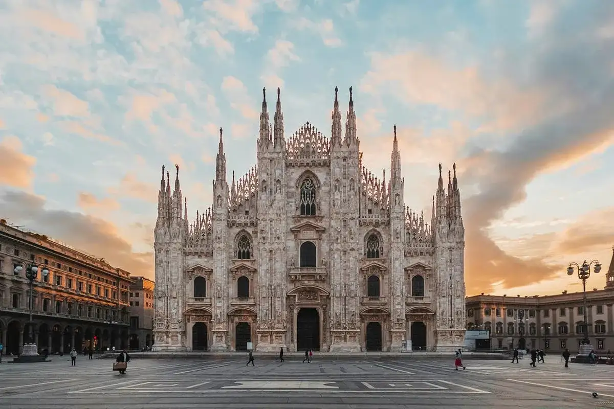 Il maestoso Duomo di Milano si erge sotto un cielo al tramonto, con le sue guglie che sfiorano le nuvole colorate.