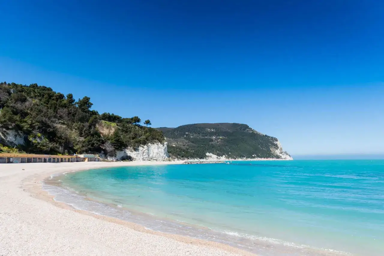 Spiaggia bianca e mare turchese nelle Marche, un bel mare da sogno con scogliere verdi e cielo azzurro.
