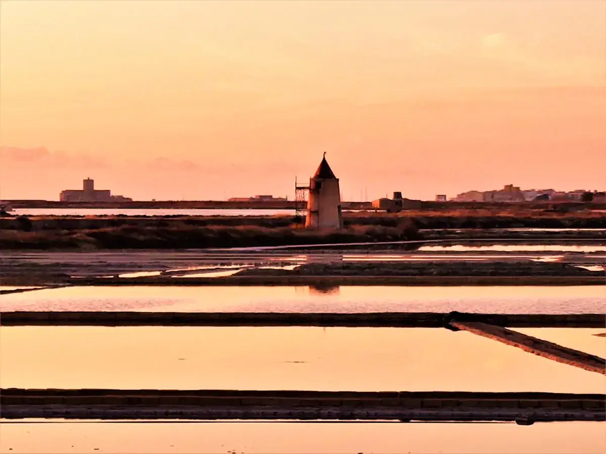 Saline di Trapani al tramonto, un mulino solitario e riflessi dorati. Un'idea per cosa vedere a Trapani in 3 giorni.
