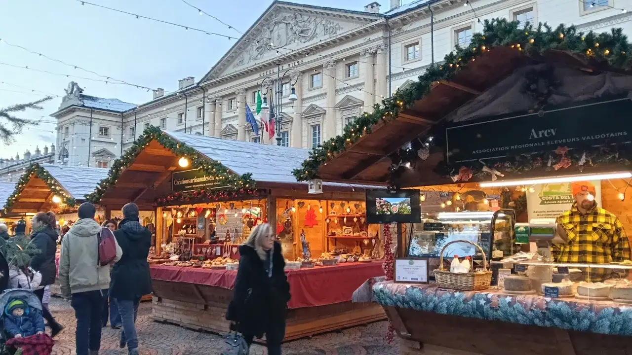 Mercatini di Natale Aosta: bancarelle illuminate con prodotti tipici e artigianato, sullo sfondo l'Hotel de Ville.